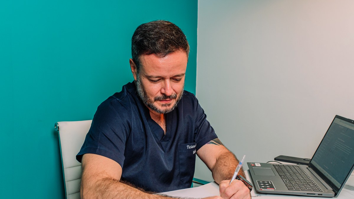 Dr. Ticiano Sampaio escrevendo em sua mesa de trabalho no consultório